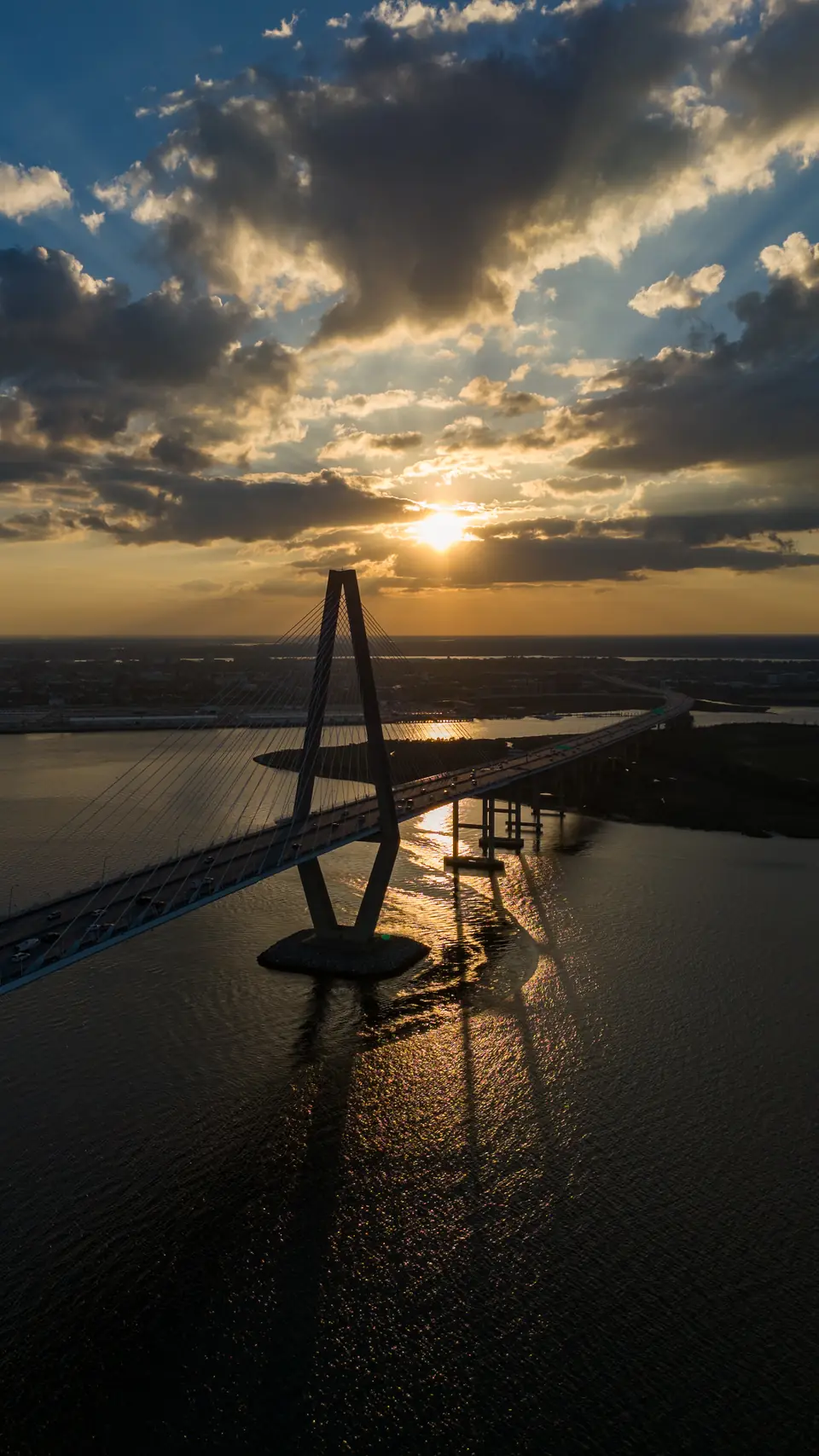 Vertical drone photo of the sun breaking through clouds above a Ravenel Bridge tower, Charleston, SC